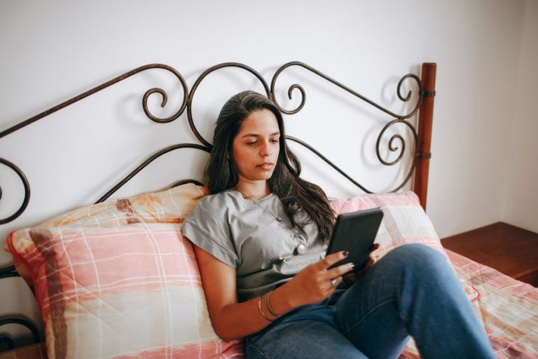 A woman relaxes on a bed using a tablet, reflecting a modern lifestyle indoors.
