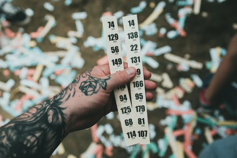 Mão tatuada segurando bilhetes de sorteio entre confetes em festa, ilustrando estratégias de loterias
