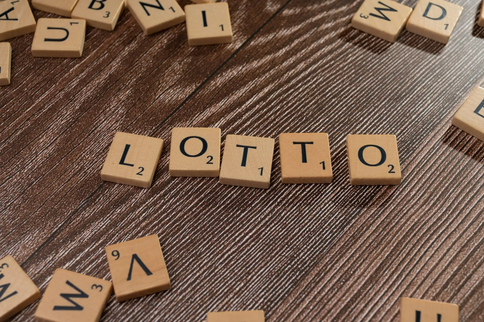Peças de Scrabble formando a palavra LOTTO sobre mesa de madeira, representando sorte e apostas